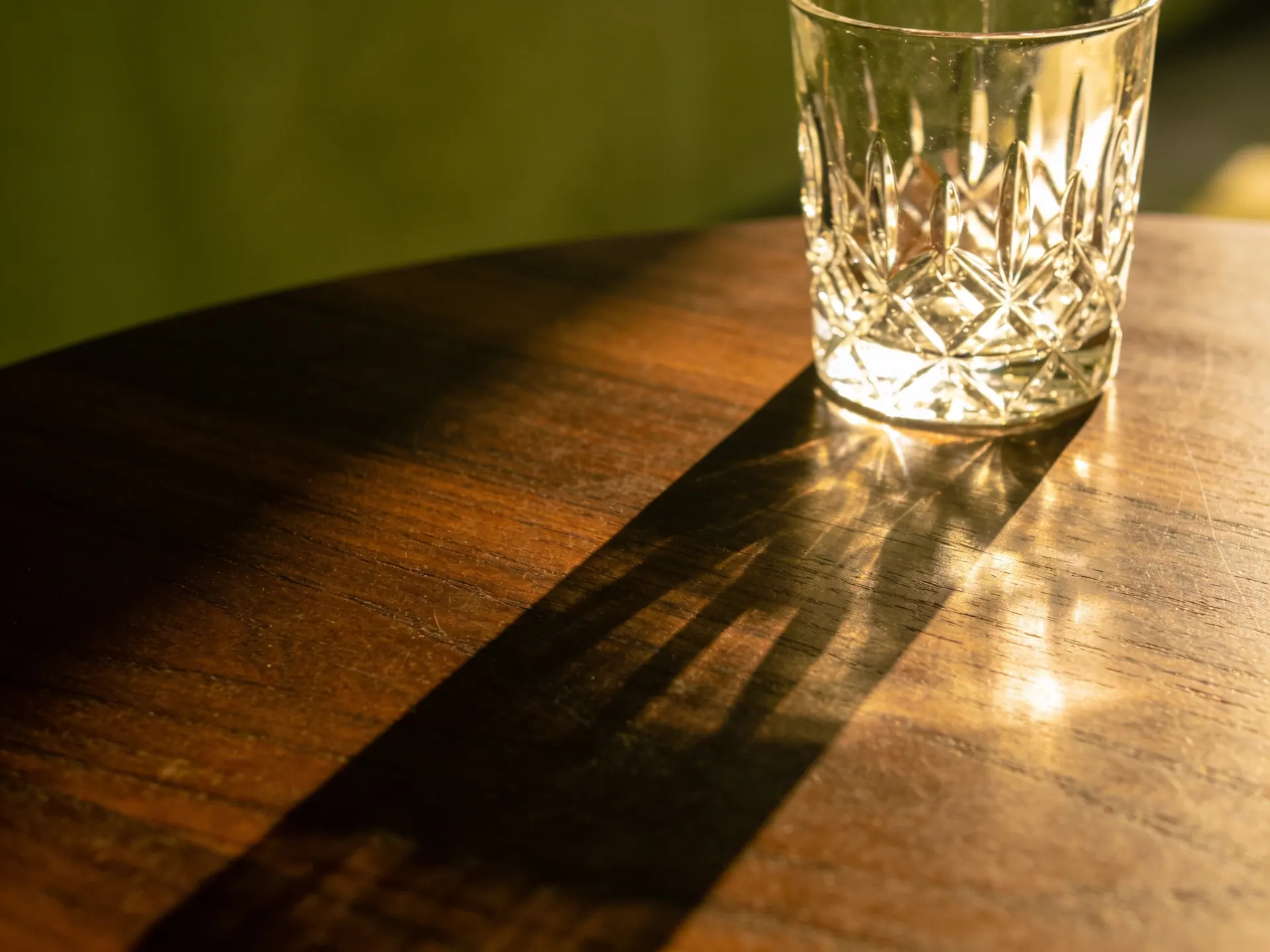 Copo de cristal sobre madeira escura polida com luz dourada de fim de tarde